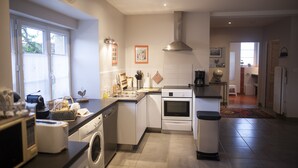 A modern kitchen with a dishwasher, oven, and sink. There is a clock on the wall and a window with blinds. - The Village cottage with outdoor pool (Normier)