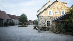 A stone building with a gravel driveway, a wooden bench, and a small garden area. - The Village cottage with outdoor pool (Normier)