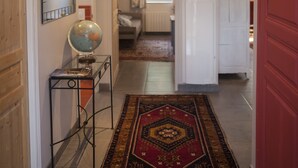 A hallway with a globe on a stand, a patterned rug, and a red door. - The Village cottage with outdoor pool (Normier)