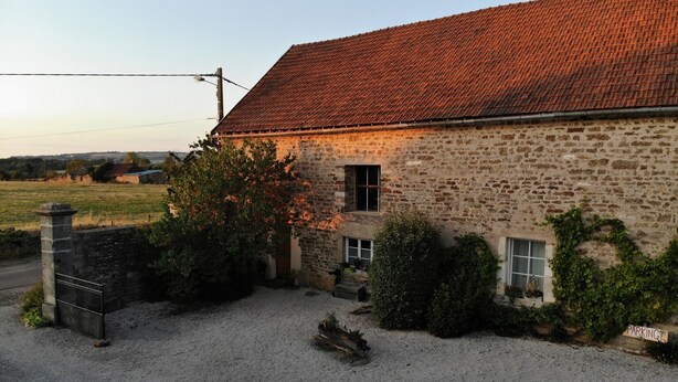 A stone building with a red-tiled roof, a gravel driveway, and a sign indicating parking. - The Village cottage with outdoor pool (Normier)