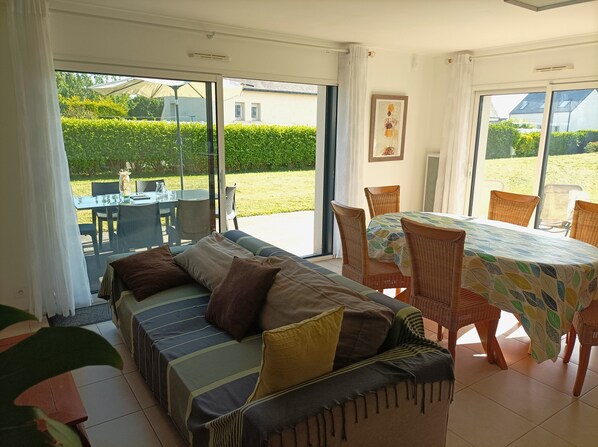 Una stanza con divano, tavolo da pranzo e sedie, con vista su un giardino attraverso ampie finestre.