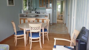 Una cocina compacta con zona de comedor, sillas de madera, televisor y refrigerador.