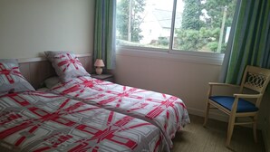 Un dormitorio con cama, una silla, una mesita de noche y una ventana con cortinas.
