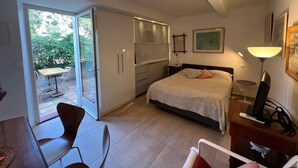 Ein Schlafzimmer mit Bett, Nachttisch, Lampe und Blick auf den Garten durch eine Schiebetür.