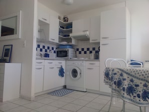 A compact kitchen with white cabinets, a microwave, a washing machine, and a sink.