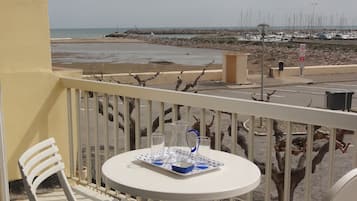 A balcony with a round table, two white chairs, and a view of the beach and marina.