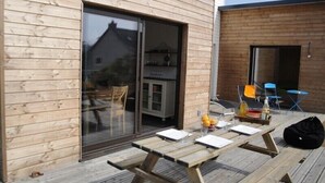 A wooden deck with a picnic table, chairs, and a glass door leading to an interior space.
