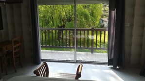 Une chambre dotée d’une grande porte-fenêtre coulissante donnant sur un balcon avec vue sur un jardin verdoyant et une clôture en bois.