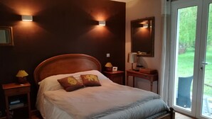 Une chambre à coucher avec un lit en bois, deux lampes de chevet, une table de nuit, un miroir et une vue sur l’extérieur grâce à une porte vitrée.