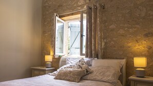 Ein Schlafzimmer mit Steinwand, einem Bett mit gemusterten Kissen, einem Fenster mit Vorhängen und Nachttischlampen.