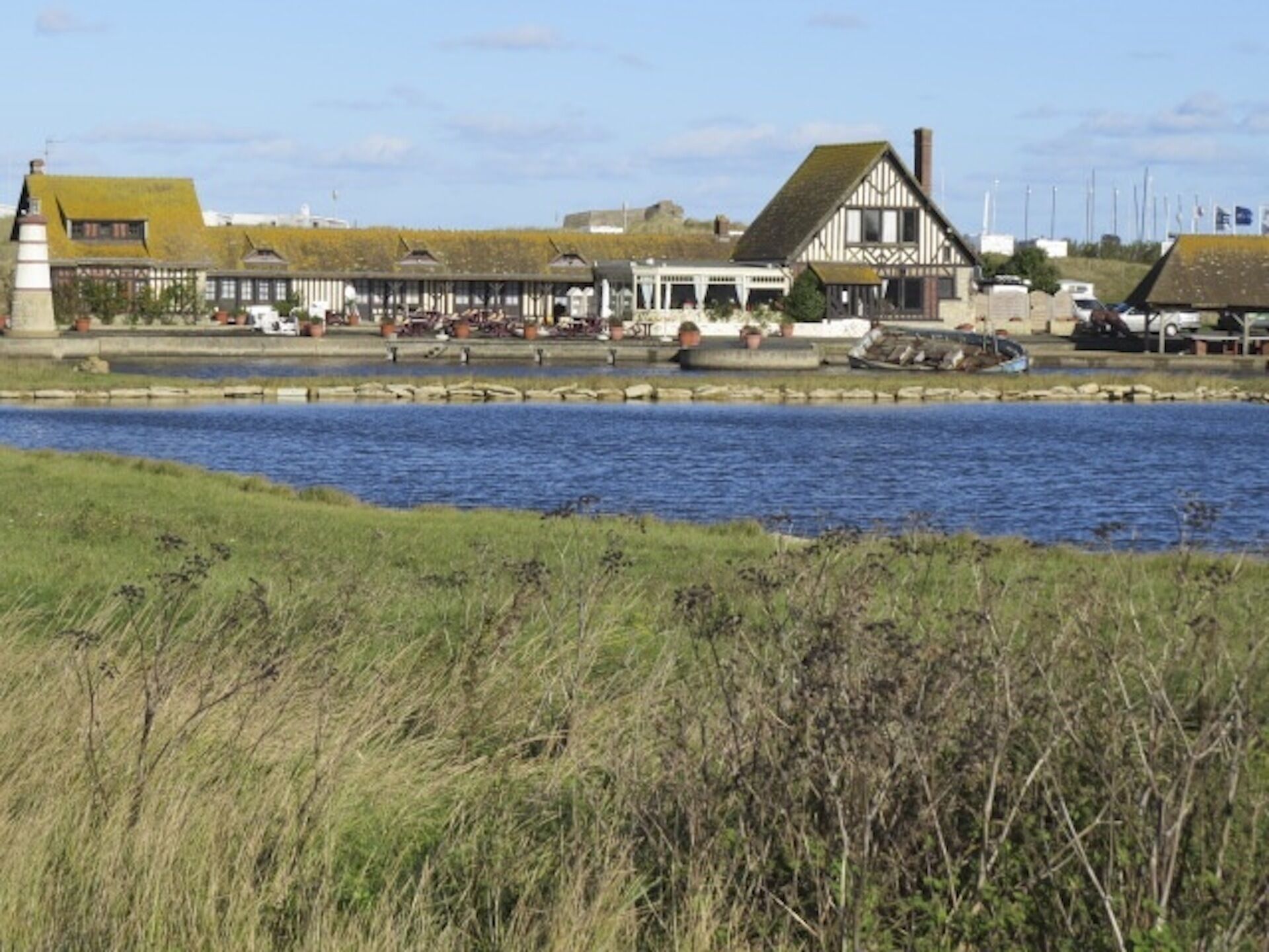 A riverside building with a traditional architectural style, a dock, and a grassy foreground.