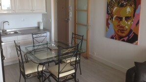 A dining area with a glass table and chairs, a kitchen with white cabinets, and a painting on the wall. - BEAUTIFUL WATERFRONT APARTMENT - BREATHTAKING MARINA AND SEA VIEWS! (Courseulles-Sur-Mer)