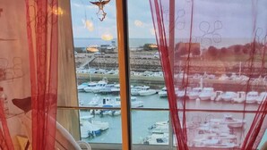 A room with a view of a marina through sheer curtains. There are two rocking chairs in the foreground. - BEAUTIFUL WATERFRONT APARTMENT - BREATHTAKING MARINA AND SEA VIEWS! (Courseulles-Sur-Mer)