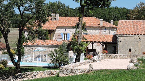 A stone building with a tiled roof, a swimming pool, and a garden area with trees and outdoor seating. - Country house with heated swimming pool with solar panels. (Mauroux)