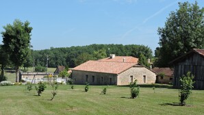 A stone building with a tiled roof, surrounded by a grassy field and trees. - Country house with heated swimming pool with solar panels. (Mauroux)