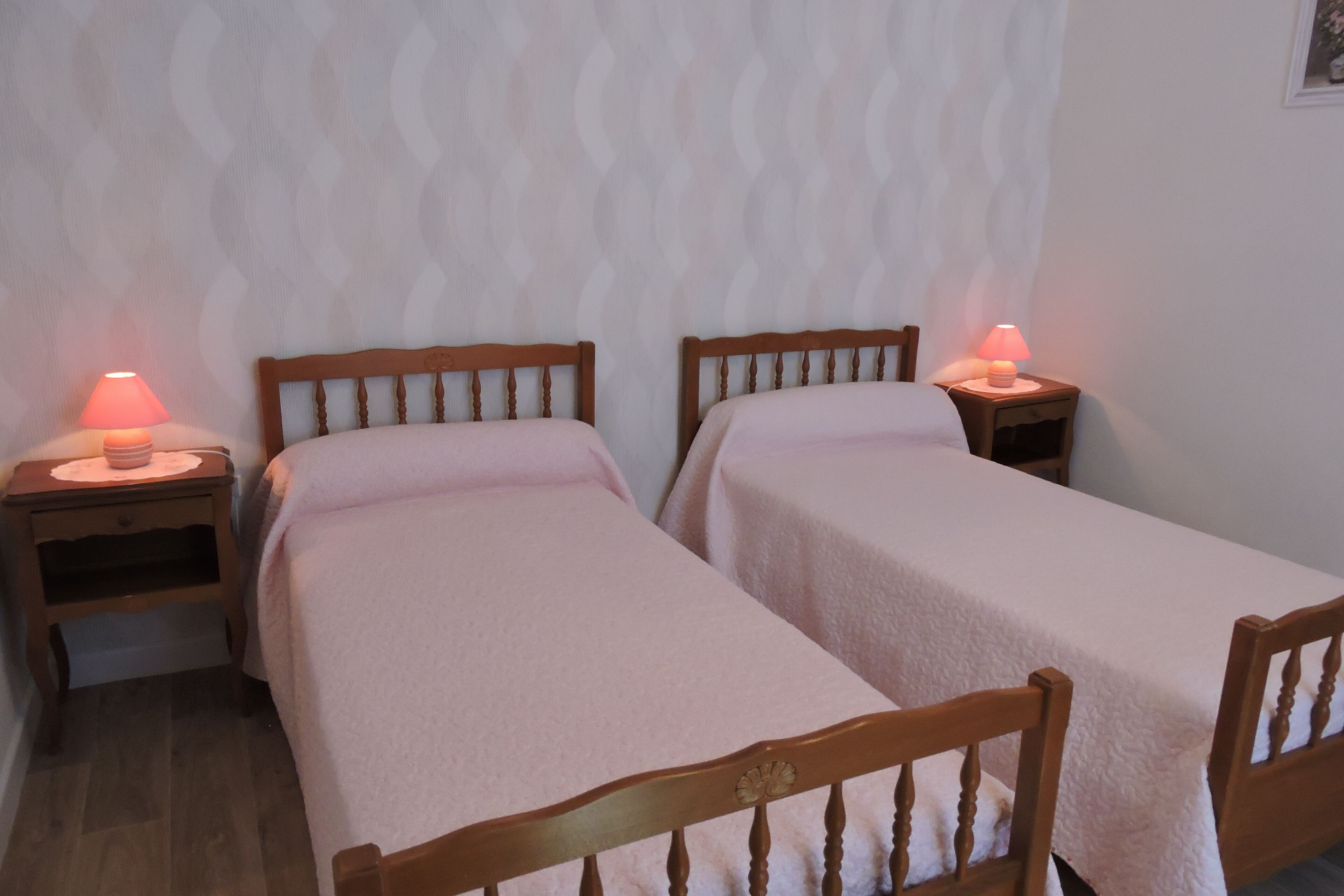 A room with two wooden beds, each with a small bedside table and a lamp.