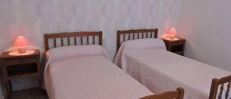 A room with two wooden beds, each with a small bedside table and a lamp.