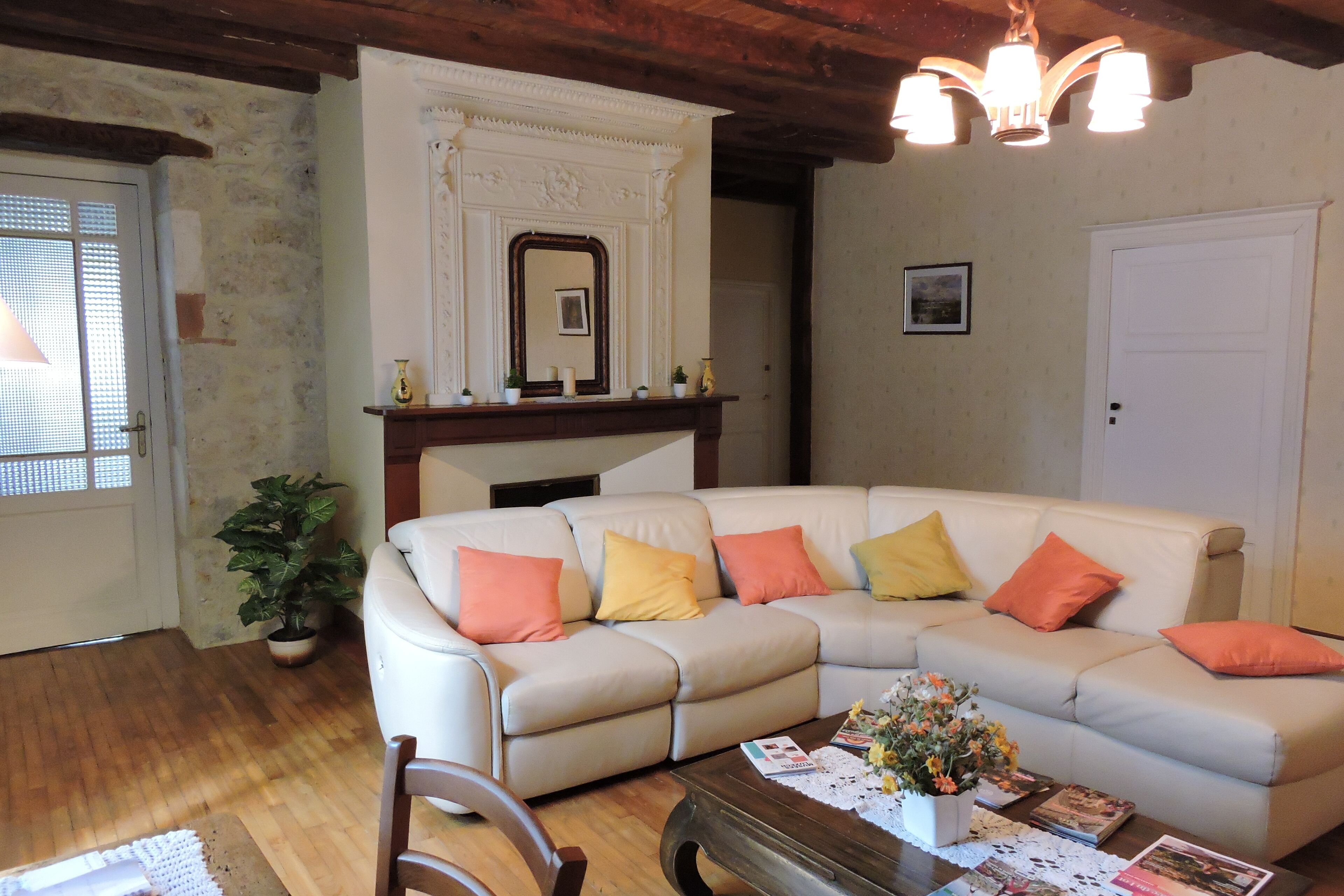 A living room with a beige sectional sofa, a wooden coffee table, a potted plant, and a fireplace with a mirror above it.
