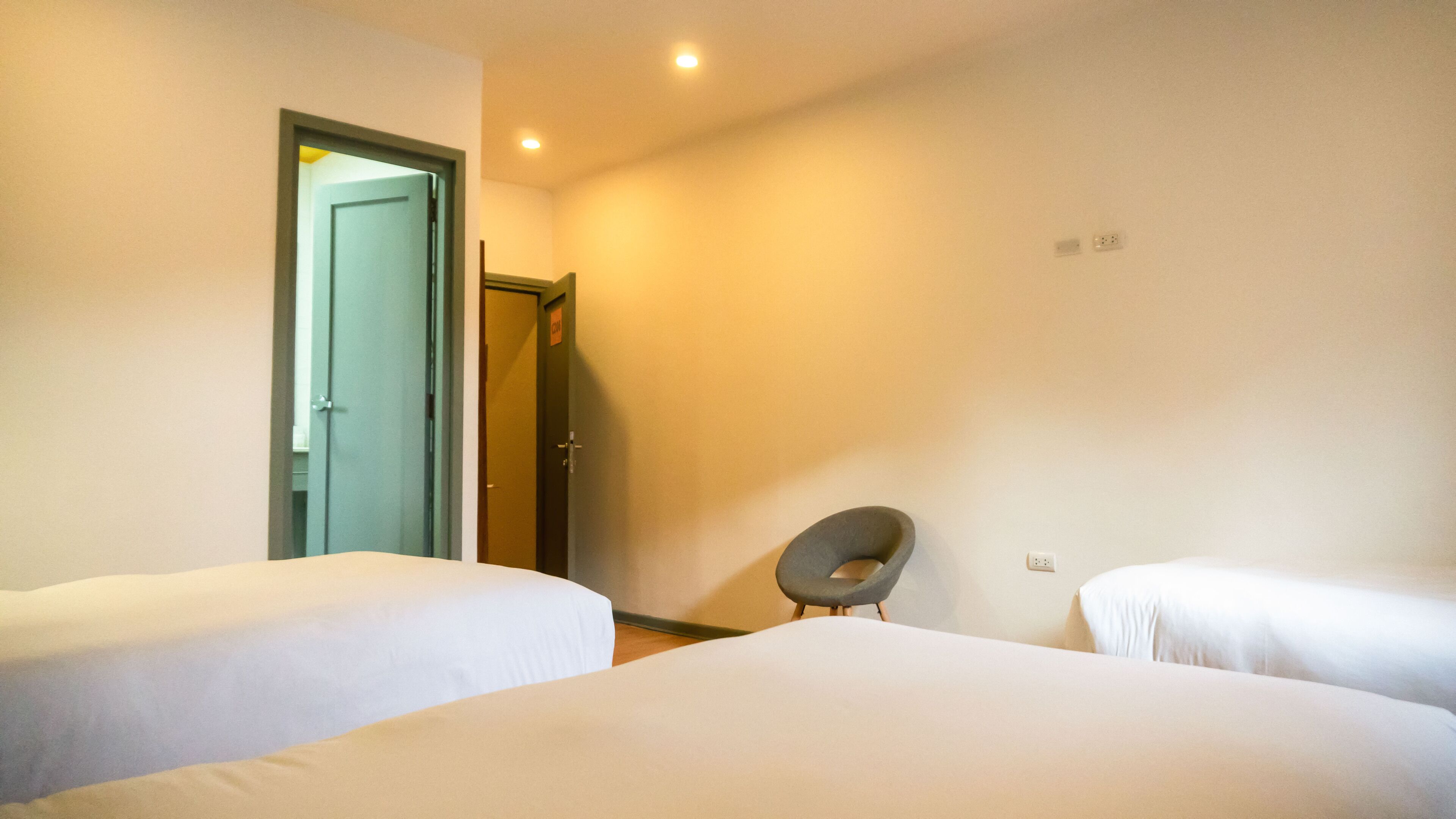 A hotel room with two beds, a chair, and a door leading to another room.
