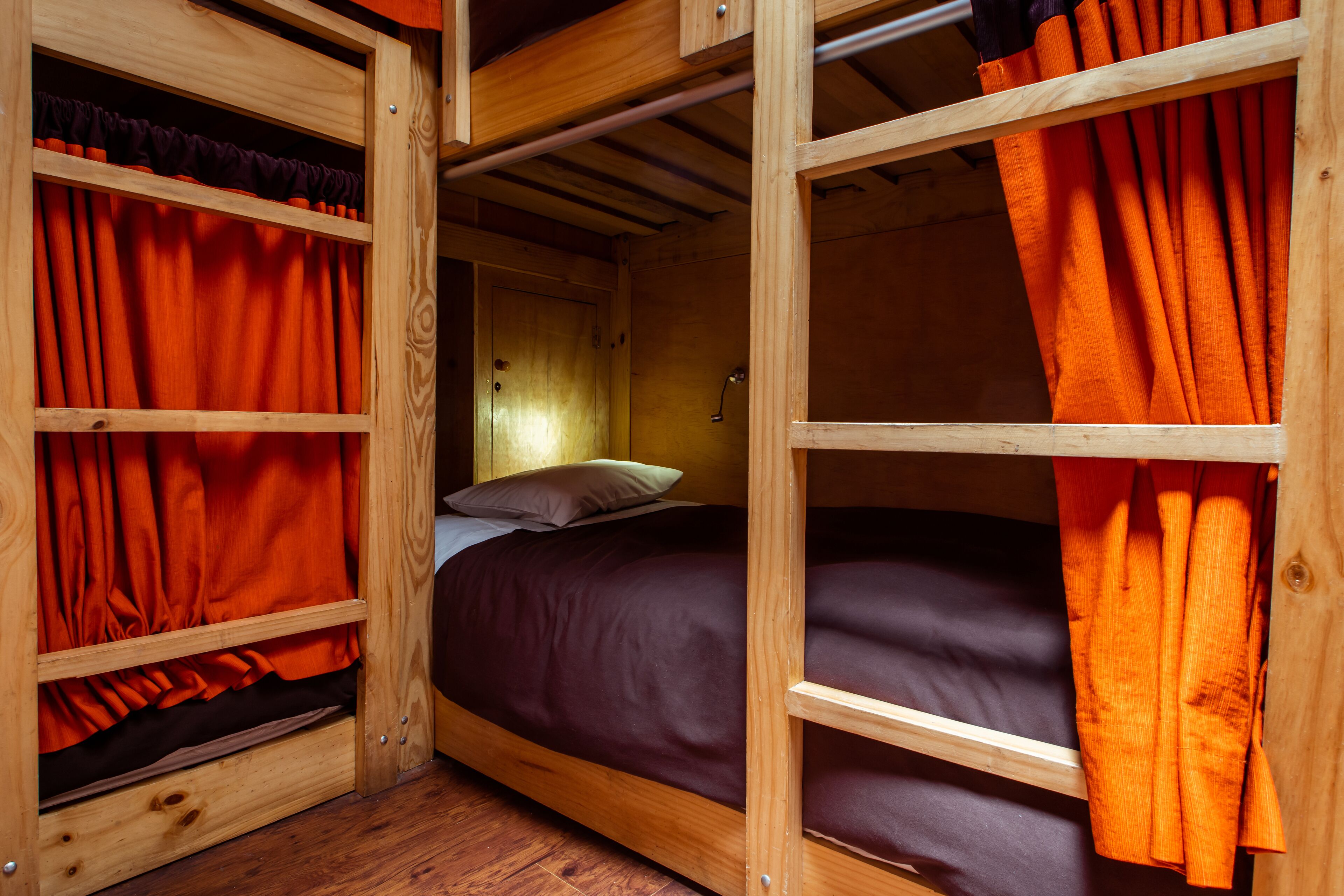 Una cama litera de madera con cortinas naranjas, cabecera de madera y suelo de madera.