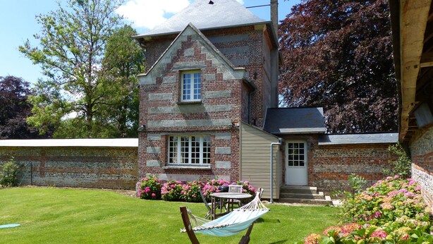 Une maison en pierre à deux étages, dotée d’une pelouse bien entretenue, d’un hamac et de parterres de fleurs.