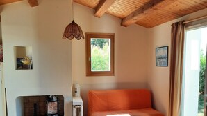 Een gezellige kamer met een houten plafond, een bank, een tafel met een kleurrijk tafelkleed en een raam met gordijnen.