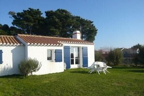 A white building with blue shutters, a tiled roof, and a small lawn area.