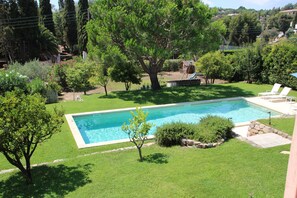 A rectangular swimming pool surrounded by a well-maintained lawn, with a large tree in the center and a small deck area with chairs. - Charming villa with pool and sea view, ideal for family or friends (Vallauris)