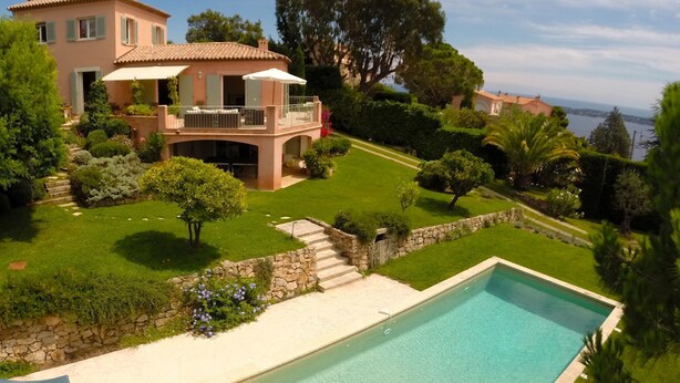 Une grande maison avec une piscine, entourée de pelouses et d’arbres bien entretenus.