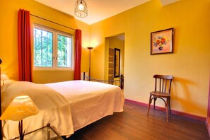 A hotel room with a bed, a chair, a lamp, a window with curtains, a painting, and a door leading to another room. - Charming villa with pool and sea view, ideal for family or friends (Vallauris)