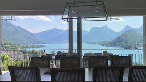 Comedor con sillas de mimbre y una mesa, con vistas a un lago y montañas.