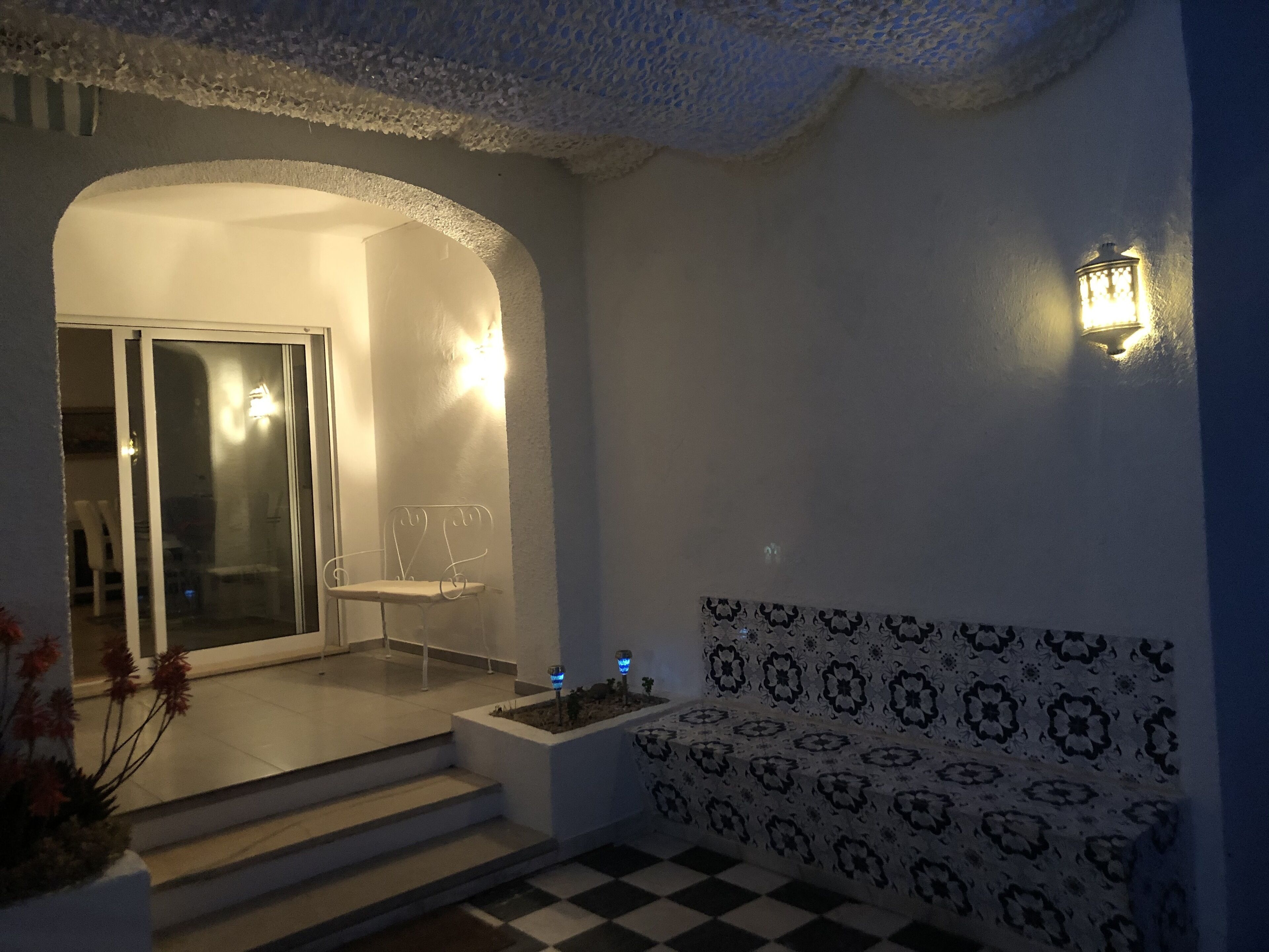 A well-lit entrance with a glass door leading to a patio area, a small seating area with a patterned wall, and a checkered floor.