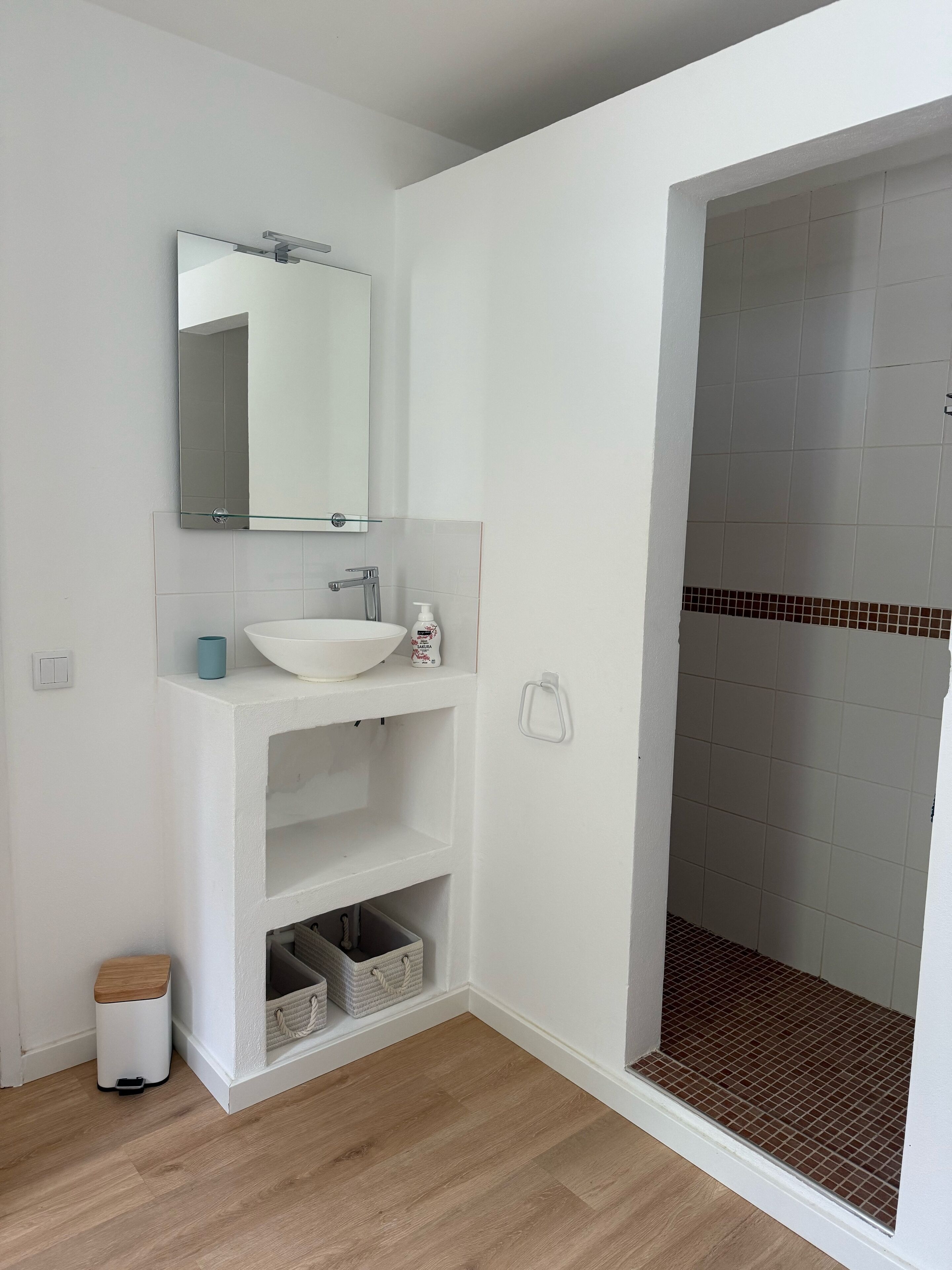 A modern bathroom with a white sink, mirror, and tiled shower area.