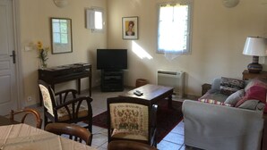 Ein Wohnzimmer mit Fernseher, einer Couch, einem Esstisch und Stühlen.