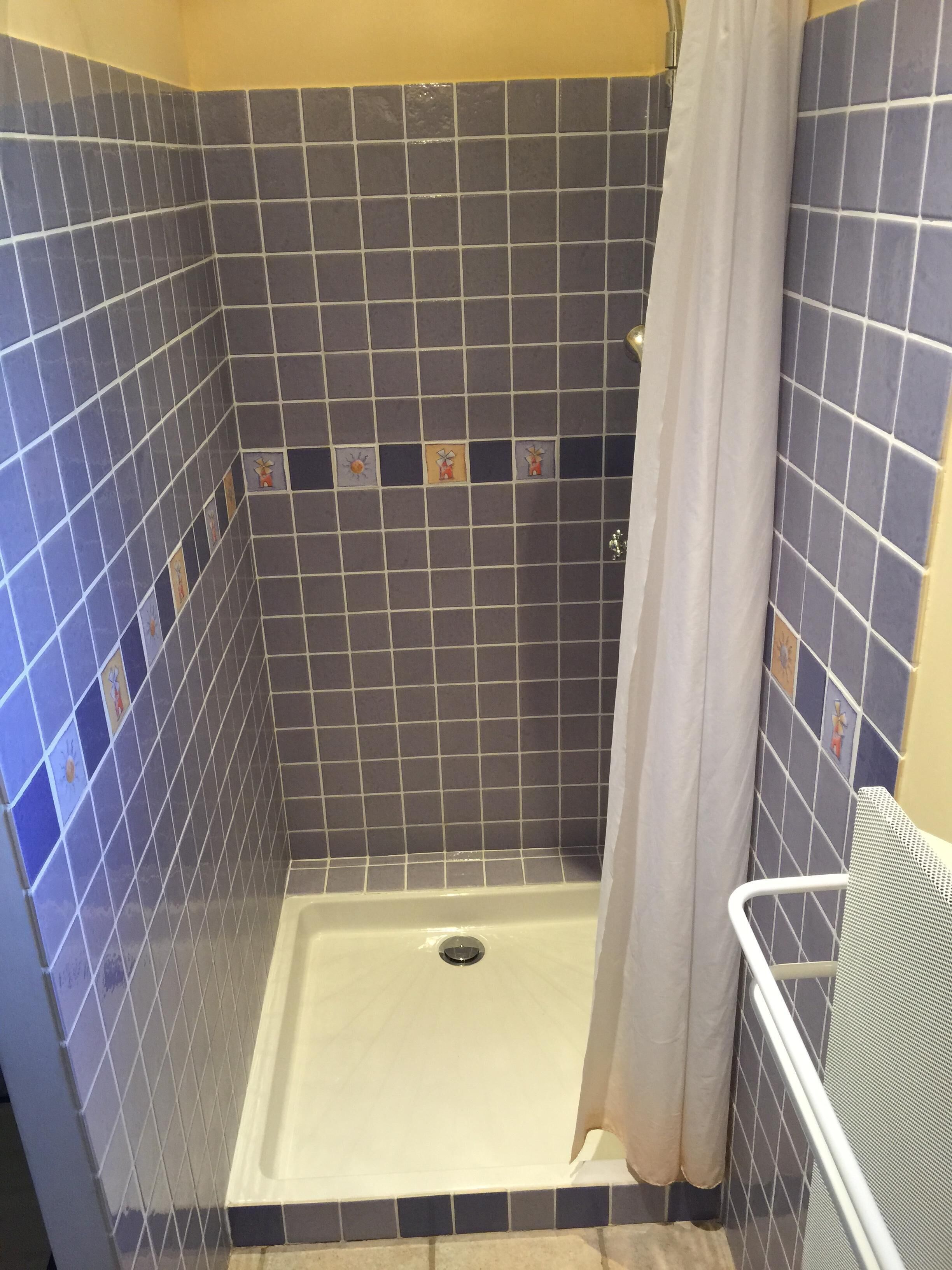Un espace douche avec des carreaux bleus et gris, un rideau de douche blanc et une barre de sécurité en métal.