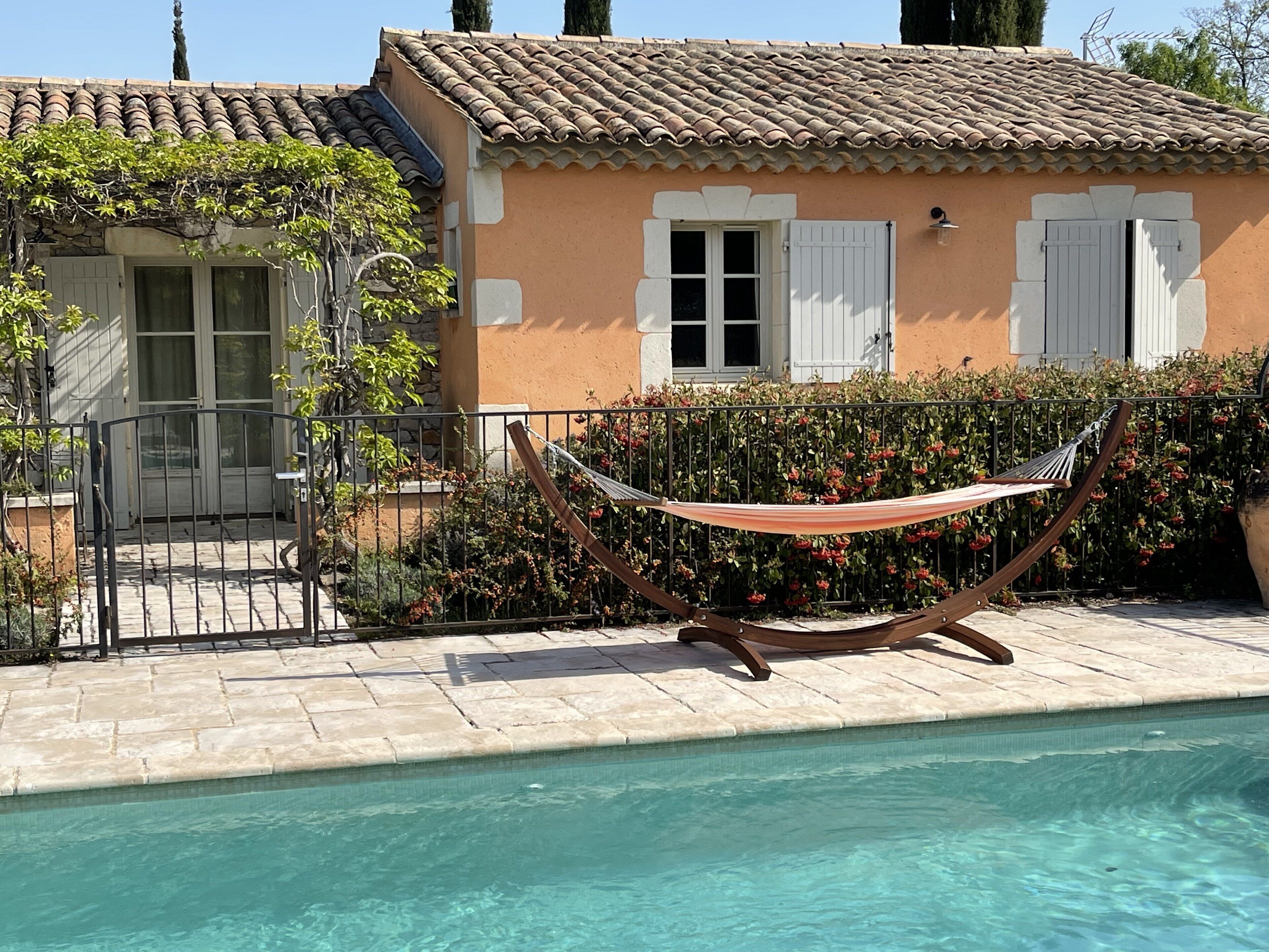 A pool area with a hammock, a house with a tiled roof, and a gate.