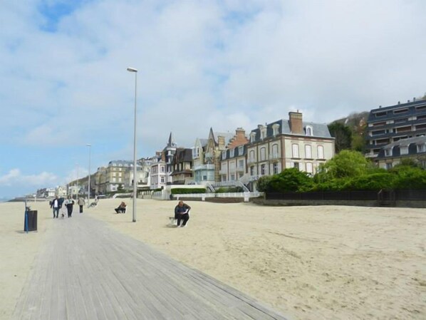 A beach with a wooden boardwalk, buildings in the background, and people walking. - Villa Mariposa - Apartment in listed villa on trouville beach (Trouville-Sur-Mer)