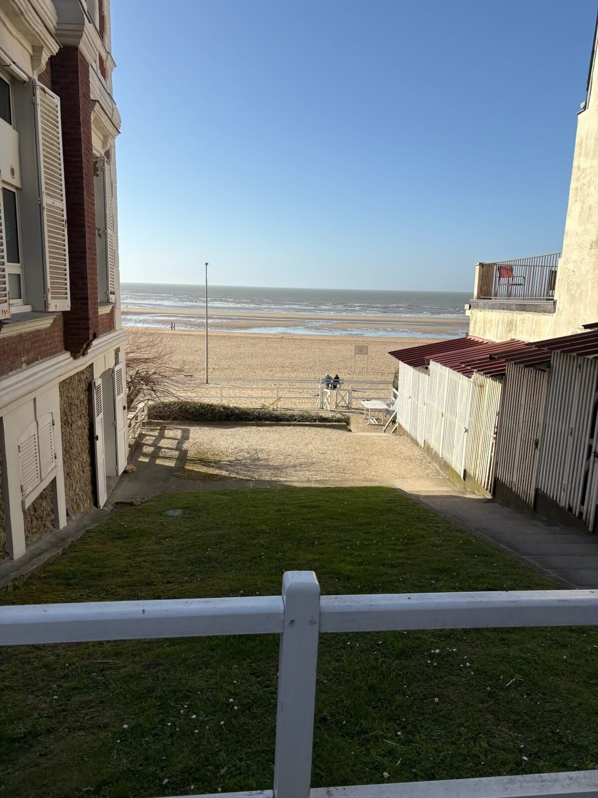 Une vue depuis un balcon donnant sur une plage, avec un ciel dégagé.