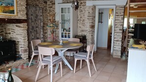 A dining area with a stone wall, a round table with yellow plates, and wooden chairs. - House "la paludière" in Rhuys Peninsula (Sarzeau)