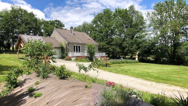 A house with a sloped roof, surrounded by a well-maintained garden with various plants and flowers. - Gîte with view of the Chaîne des Puys - 4 pers - large garden - near Vulcania (Landogne)