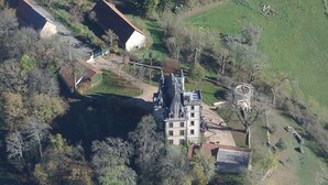 An aerial view of a large, multi-story building with a prominent tower, surrounded by trees and open fields. - Gîte with view of the Chaîne des Puys - 4 pers - large garden - near Vulcania (Landogne)