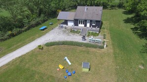 An aerial view of a house with a driveway, a patio with benches, and a small garden area. - Gîte with view of the Chaîne des Puys - 4 pers - large garden - near Vulcania (Landogne)