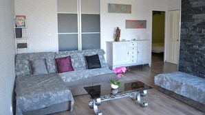 A modern living room with a grey patterned sofa, a glass coffee table, and a white cabinet. - Gîte with view of the Chaîne des Puys - 4 pers - large garden - near Vulcania (Landogne)