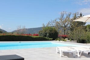 Ein Swimmingpool mit Liegestühlen und Sonnenschirm, umgeben von gepflegten Gärten und Bäumen.