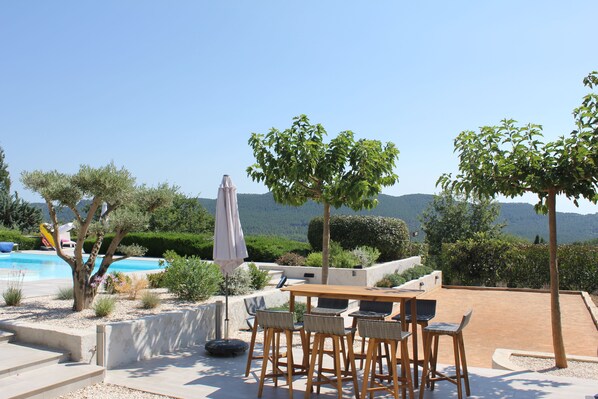 An outdoor patio with a wooden table and chairs, a pool, and a view of the mountains.