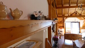A wooden interior with a shelf holding decorative items, a table with a red tablecloth, and a view of a dining area. - Beautiful duplex of 110 m² in a chalet style Full of charm, awarded 3 stars (Théus)