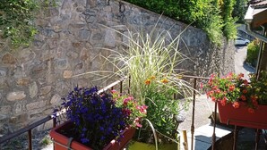 A balcony with potted plants, a stone wall, and a view of a road and greenery. - Beautiful duplex of 110 m² in a chalet style Full of charm, awarded 3 stars (Théus)