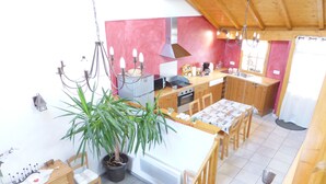 A spacious kitchen with wooden cabinets, a dining area with a table and chairs, and a potted plant. - Beautiful duplex of 110 m² in a chalet style Full of charm, awarded 3 stars (Théus)