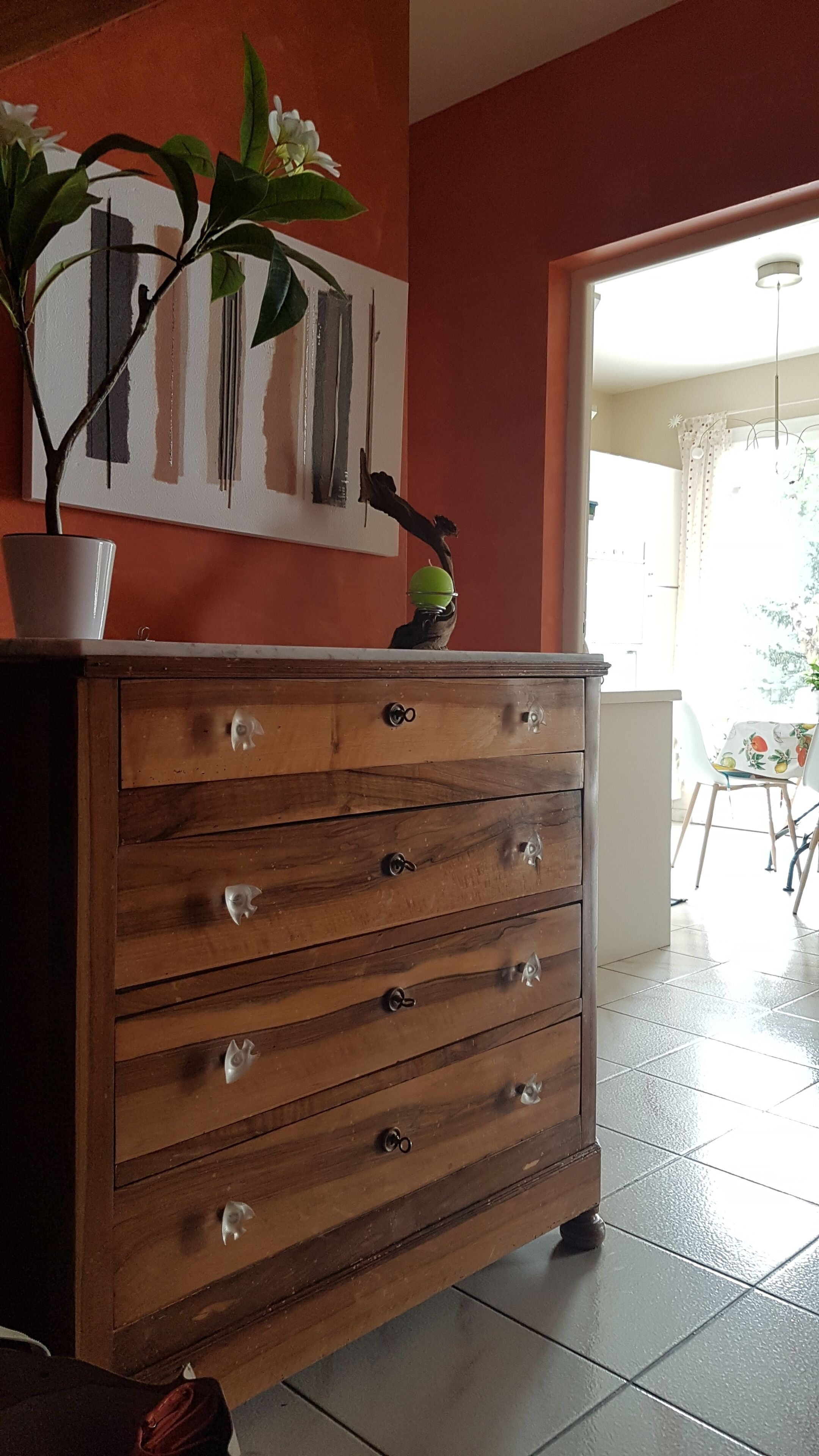 A wooden dresser with drawers, a potted plant, and a painting on the wall.