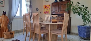 Un coin repas comprenant une table ronde, six chaises en bois, un cygne décoratif, un buffet en bois et une plante en pot.